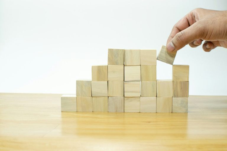 Dein individuelles PKV Konzept wird entwickelt. Eine Hand stapelt präzise Holzklötze aufeinander, was die maßgeschneiderte Entwicklung eines individuellen PKV-Konzepts symbolisiert.