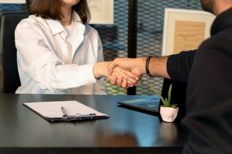 Deine langfristige Betreuung und Optimierung Eine Frau und ein Mann schütteln sich am Schreibtisch über einem unterschriebenen Vertrag die Hand zur laufenden Betreuung des PKV Konzepts.