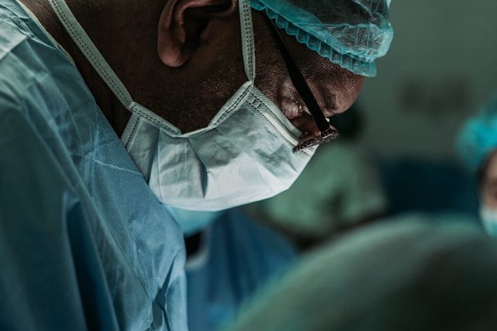 Deine erstklassige medizinische Versorgung als Selbstständiger Ein Arzt im OP-Kittel führt eine Operation durch, was den Zugang zu erstklassiger medizinischer Versorgung für Selbstständige symbolisiert.
